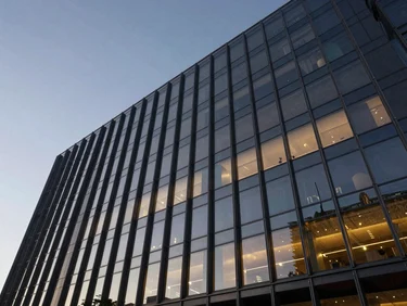 Wide angle, dramatic edge-lit architectural shot of a modern corporate headquarters facade at dusk, deep obsidian glass reflecting gold ambient light, sharp geometric steel frames, negative space on the left.