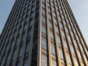 Wide-angle architectural close-up of a modern skyscraper facade, sharp steel lines reflecting golden hour light, dramatic edge-lit contrast, premium corporate aesthetic.