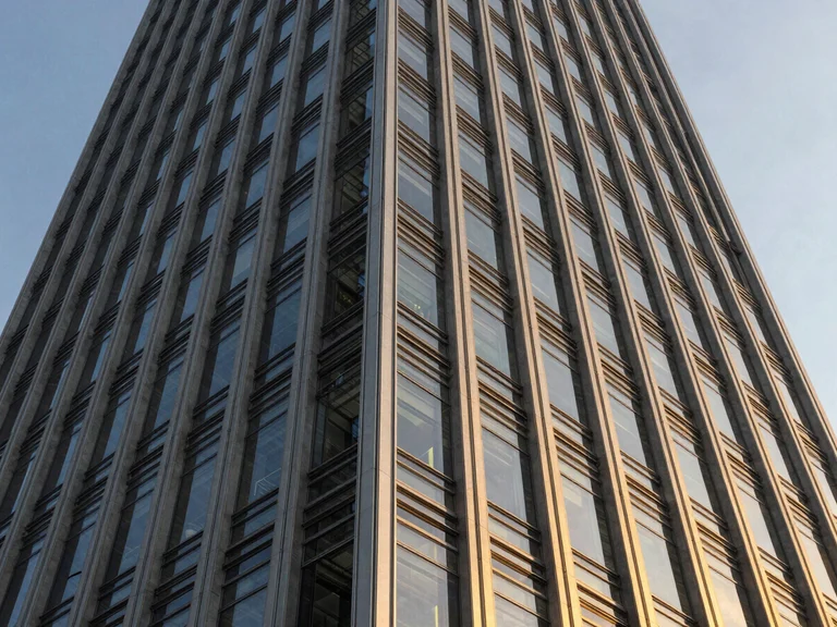 Wide-angle architectural close-up of a modern skyscraper facade, sharp steel lines reflecting golden hour light, dramatic edge-lit contrast, premium corporate aesthetic.