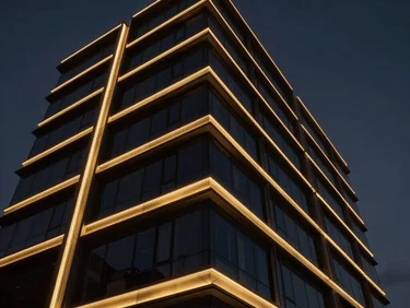 Dramatic low-angle view of a modern building facade illuminated by precise gold architectural linear luminaires, dark moody twilight sky