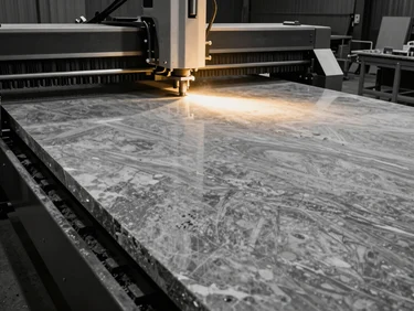 Industrial waterjet cutting machine processing a large slab of grey marble in a modern stone fabrication facility